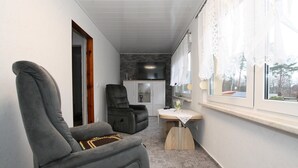 Un couloir étroit avec un fauteuil gris, un fauteuil inclinable noir et une petite table sur laquelle se trouve un vase.