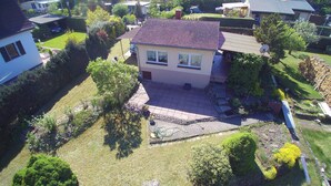 Une maison à deux étages, avec un toit recouvert de tuiles, entourée d’un jardin bien entretenu et de maisons voisines.