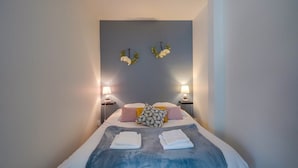 A neatly made bed with a blue blanket, two bedside lamps, and decorative wall hangings. - Les Perlières: close to the beach, center (Arcachon)