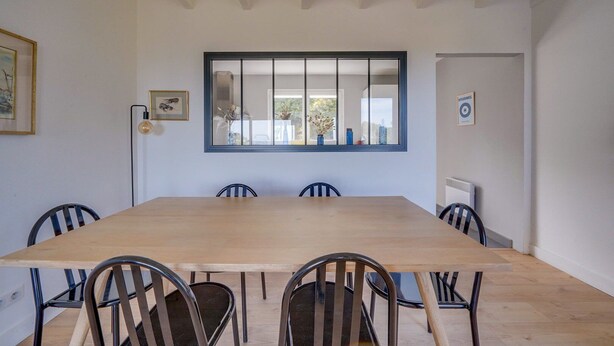 A dining room with a large wooden table and six chairs. There is a large window with a view of the outdoors.