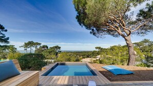 A wooden deck with a hot tub, a lounge chair, and a table with glasses.