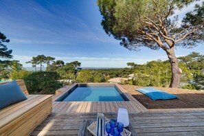 Une terrasse en bois avec un jacuzzi, une chaise longue et une table avec des verres.
