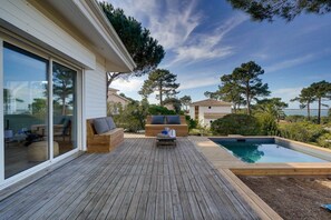 A wooden deck with outdoor furniture, a swimming pool, and a view of the sea.