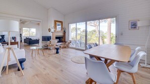 A spacious living area with a large wooden table and white chairs, a fireplace, and a view of the outdoors. - Villa Belvédère: pool, and beach 5 minutes- Pyla (La Teste-de-Buch)