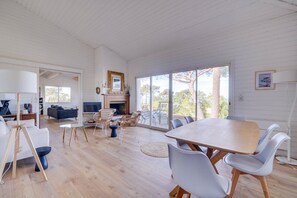 A spacious living area with a large wooden table and white chairs, a fireplace, and a view of the outdoors.