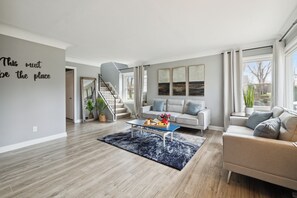 A modern living room with a staircase, a sofa, a coffee table, and artwork on the wall. - Spacious 7-bedroom house with WiFi and MASSIVE backyard in marvelous Plymouth (Plymouth)