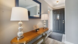 A hallway with a wooden console table, two wall-mounted lamps, a mirror, and a door with a doormat. - Spacious 7-bedroom house with WiFi and MASSIVE backyard in marvelous Plymouth (Plymouth)