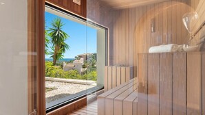 A modern bathroom with a wooden interior, a glass door leading to a balcony with a view of palm trees and buildings. - Villa Sereno | Ref. #96 (Marbella)