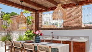 An outdoor kitchen with a bar area, wicker chairs, a sink, and hanging light fixtures. - Villa Sereno | Ref. #96 (Marbella)