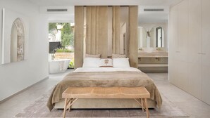 A modern bedroom with a large bed, a bedside table, a built-in bench, and a large mirror. - Villa Sereno | Ref. #96 (Marbella)