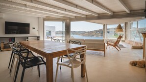 A spacious room with a large wooden table, multiple chairs, a sofa, and a view of the sea. - Villa Delta Ornos - MG Villas Mykonos (Mykonos)