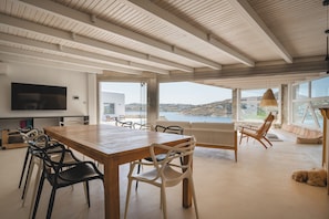 A spacious room with a large wooden table, multiple chairs, a sofa, and a view of the sea.