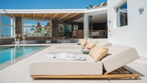 A modern poolside area with lounge chairs, a stone wall, and a clear view of the pool. - Villa Delta Ornos - MG Villas Mykonos (Mykonos)