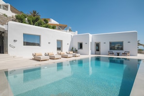 A modern pool area with white walls, multiple lounge chairs, and a clear blue pool.