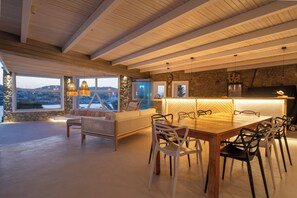 Un vaste espace de salle à manger avec une table et des chaises en bois, un canapé avec des coussins et de grandes fenêtres offrant une vue sur le paysage.