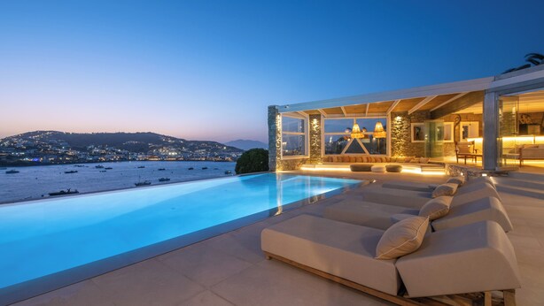 A modern poolside area with lounge chairs and a view of the sea and distant hills. - Villa Delta Ornos - MG Villas Mykonos (Mykonos)