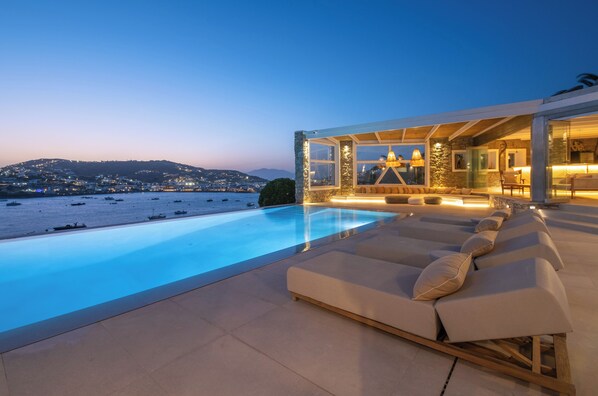 A modern poolside area with lounge chairs and a view of the sea and distant hills.
