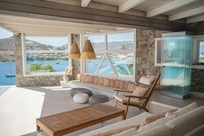 A modern interior with a stone wall, large windows, a wooden table, and a seating area with cushions.