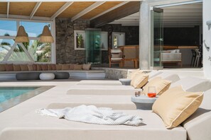 Un espace de détente extérieur moderne, doté d’une piscine, de sièges confortables et d’une porte vitrée donnant accès à une salle à manger.