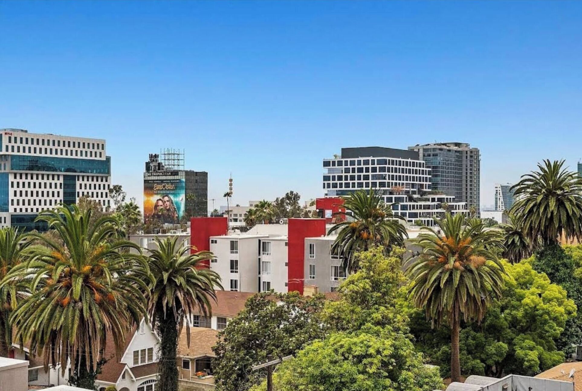 Un paysage urbain avec des bâtiments modernes, des palmiers et un ciel dégagé.