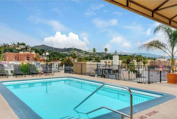 A swimming pool with a metal railing, surrounded by a fence, and overlooking a residential area with hills in the background.