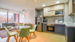 A modern kitchen with a built-in microwave, oven, and refrigerator. There is a dining area with a round table and chairs. - Nuevo y hermoso depto central en Pucón (Pucon)