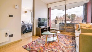 A modern living room with a large window, a sofa, a TV, and a small table. - Nuevo y hermoso depto central en Pucón (Pucon)