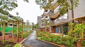 A pathway flanked by raised garden beds and wooden structures, leading to a modern building with balconies. - Nuevo y hermoso depto central en Pucón (Pucon)
