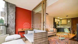 A modern living room with a sofa, a dining area with chairs, a kitchen in the background, and a stone wall. - Nuevo y hermoso depto central en Pucón (Pucon)