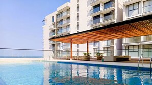 A modern hotel with a swimming pool, outdoor seating, and a view of the sea.