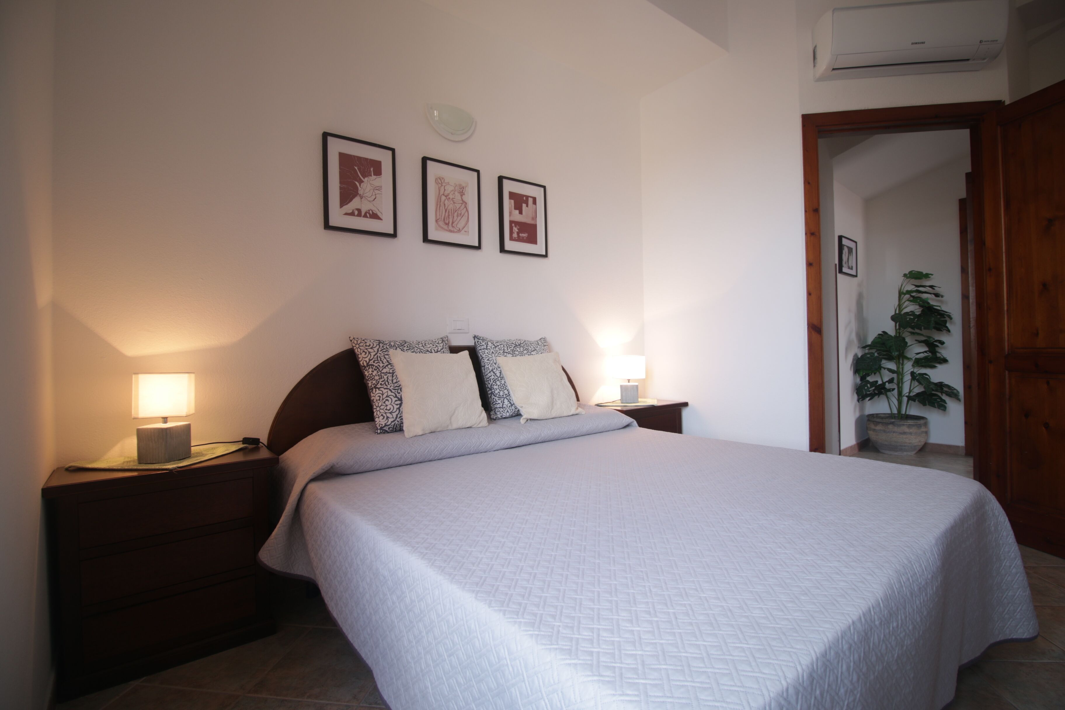 Un dormitorio con cama, mesitas de noche, lámpara y cuadros en la pared.