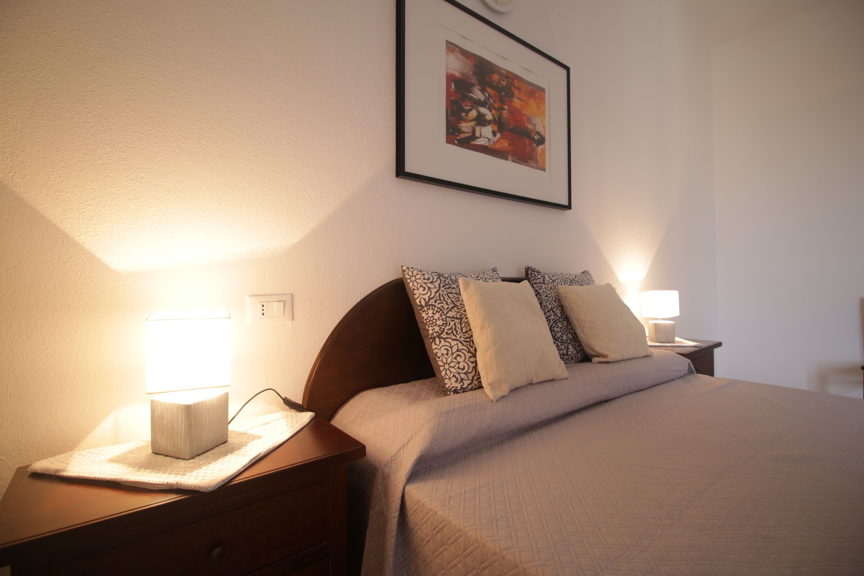 Un letto rifatto con copripiumino trapuntato e cuscini decorati, affiancato da comodini con lampade, in una stanza con un quadro appeso alla parete.