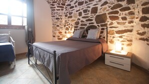 Una camera da letto con parete in pietra, un letto con testiera, un comodino con una lampada e una sedia.