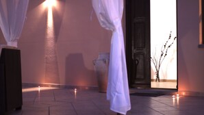 Un corridoio poco illuminato con pavimento piastrellato, un vaso grande e una porta che dà su un'altra stanza.