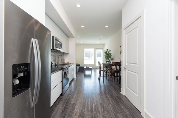 A modern kitchen with stainless steel appliances, a dining area with a table and chairs, and a hallway leading to a door. - 2BR Hollywood Apt w/ Rooftop deck & Stunning Views (Los Angeles)