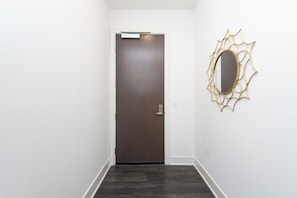 A hallway with a dark wooden door, a white wall, and a gold-framed mirror. - 2BR Hollywood Apt w/ Rooftop deck & Stunning Views (Los Angeles)