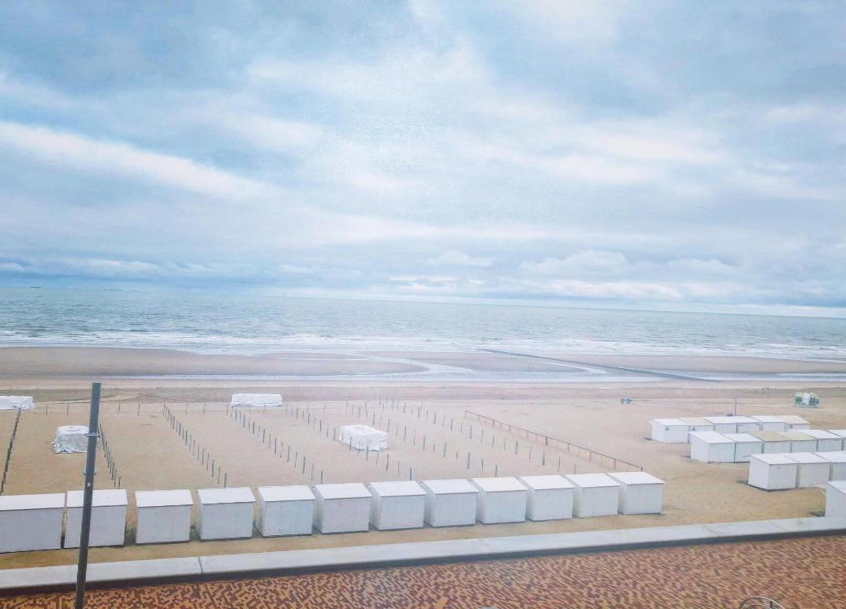 A beach with a sandy area and a series of white structures, possibly beach huts or storage units, arranged in rows.