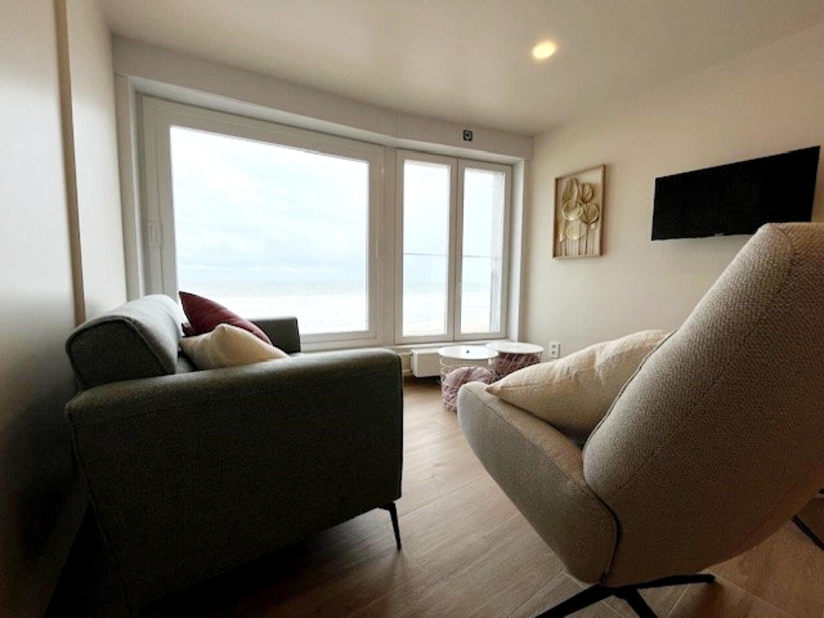 A modern living room with a sofa, armchair, and a large window offering a view.
