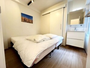 A small, neatly arranged bedroom with a single bed, a bathroom with a mirror and sink, and a picture of wheat on the wall. - Apartment in Wenduine With Stunning Sea Views (De Haan)
