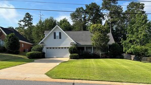 A two-story house with a garage, surrounded by well-maintained lawns and trees. - Large private home near campus (Auburn)