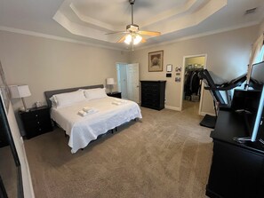 A bedroom with a bed, a dresser, a treadmill, and a closet.