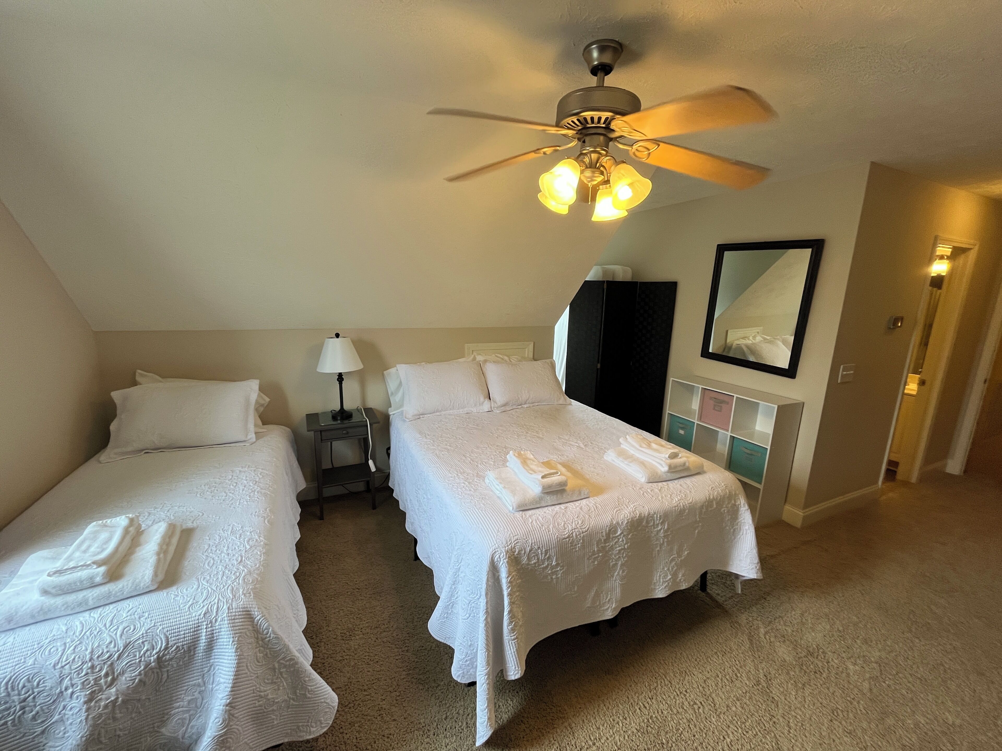 Une chambre d’hôtel avec deux lits, un ventilateur de plafond, une table de chevet avec une lampe, une armoire et un miroir au mur.