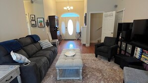 A living room with a sofa, ottoman, and chairs, a ceiling fan, and a TV. - Large private home near campus (Auburn)