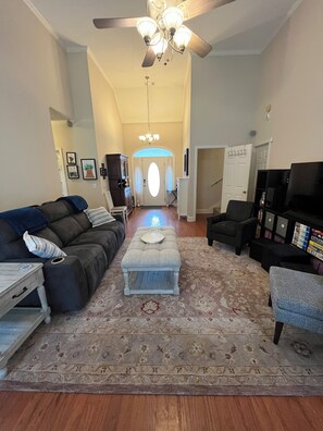 A living room with a sofa, ottoman, and chairs, a ceiling fan, and a TV.