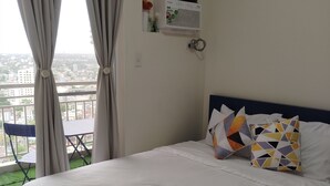 Un dormitorio con cama, almohadas, cortinas, una ventana y vistas a la ciudad.