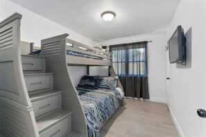 A compact room with a bunk bed, a small desk, and a television mounted on the wall.