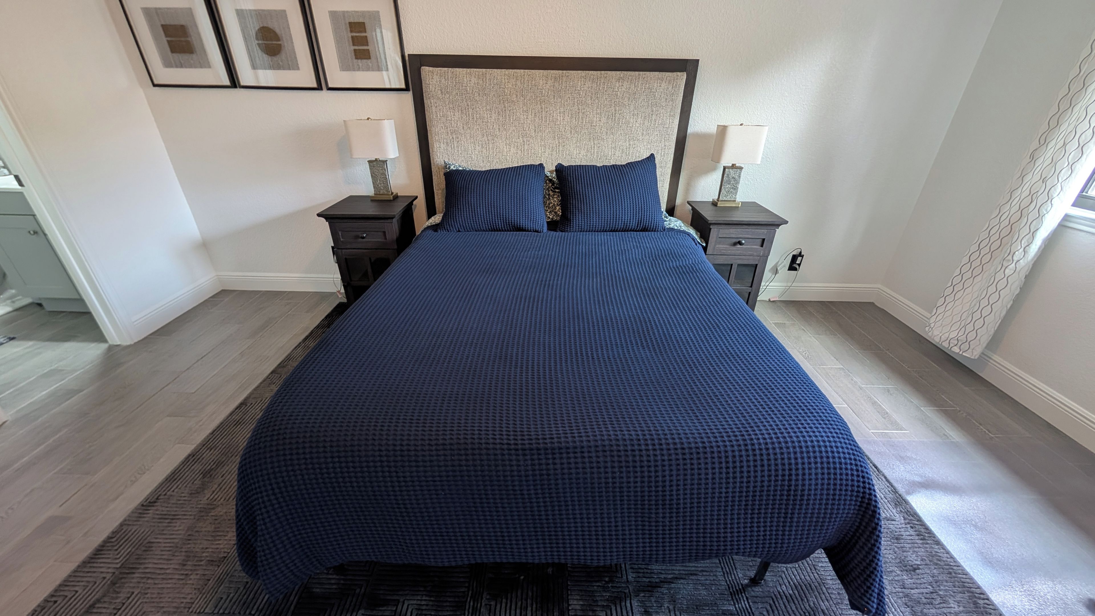 Une chambre à coucher avec un grand lit, deux tables de chevet avec des lampes, une tête de lit et un tapis à motifs.