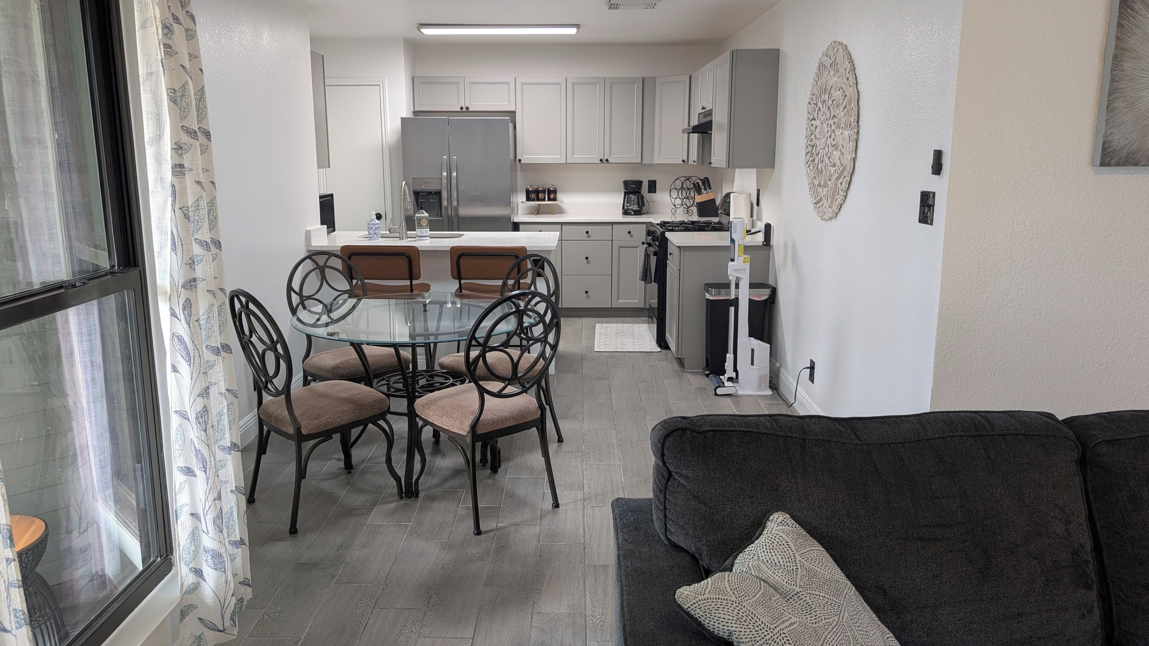 Una cocina moderna con armarios blancos, un refrigerador de acero inoxidable y un comedor con mesa de vidrio y sillas de metal.