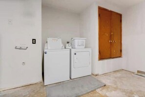 A laundry room with a washing machine and dryer, a wooden wardrobe, and a small mat on the floor.