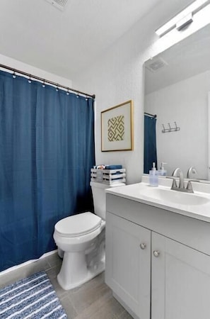 Un baño con inodoro blanco, lavabo con espejo y cortina de ducha azul.